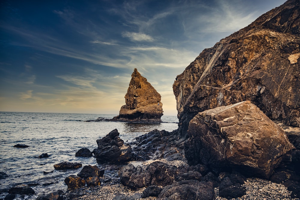 brown rock formation on sea under blue sky during daytime