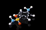 A molecular model composed of various colored spheres connected by rods, representing atoms and bonds. The model is placed against a black background, highlighting the vibrant colors of the spheres including blue, yellow, orange, and white.