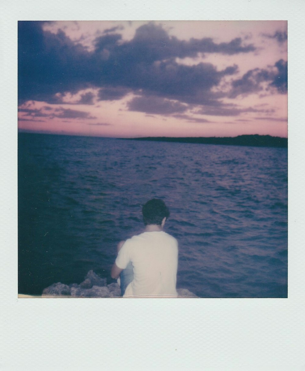 man in white shirt sitting on rock near body of water during daytime