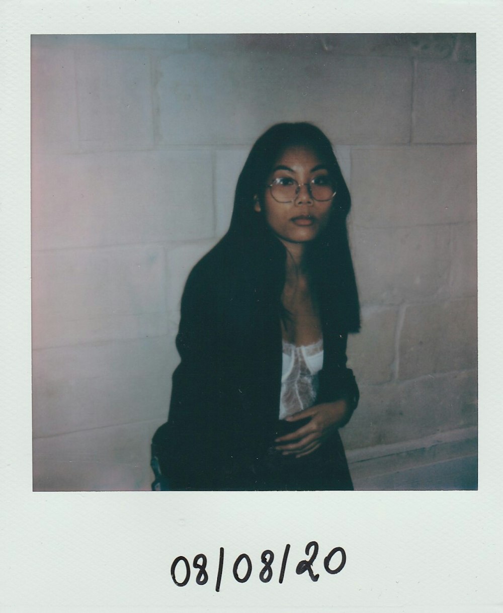 a woman wearing glasses standing in front of a brick wall