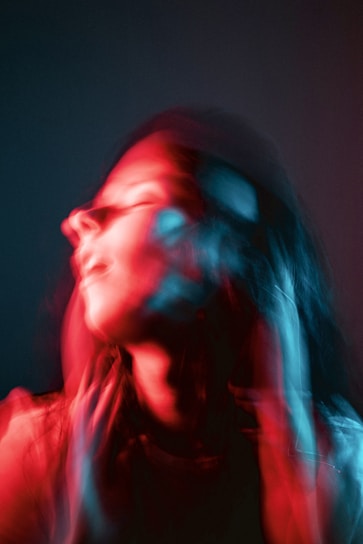 A blurred portrait of a person with motion capturing an abstract effect combining red and blue lighting, giving it a dynamic feel. The face and features are indistinct due to the motion blur, creating a sense of movement and vividness.