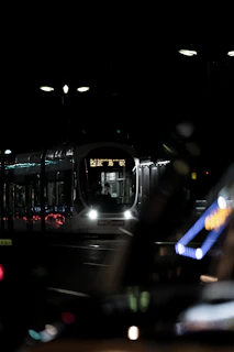 Evening exterior of a modern tram system gliding smoothly along urban tracks with city lights reflecting on steel surfaces