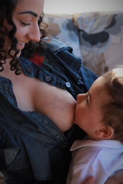 A tender moment between a mother and her baby as she breastfeeds. The mother is wearing a denim shirt and is smiling as she gazes at the baby, who is wrapped in white clothing and looking up at her.