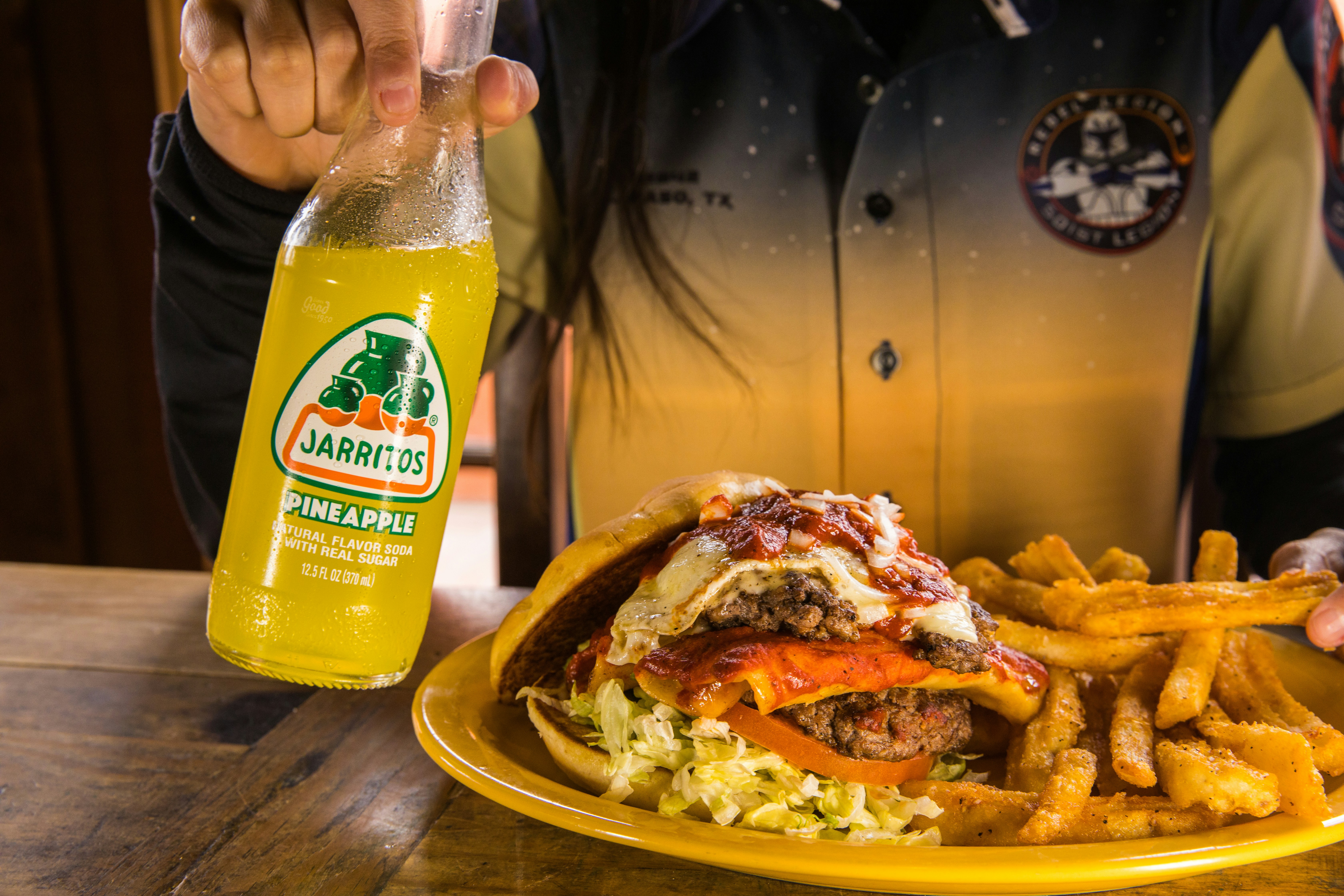 burger and fries on brown wooden table, Jarritos Pineapple being enjoyed with Tamale Burger