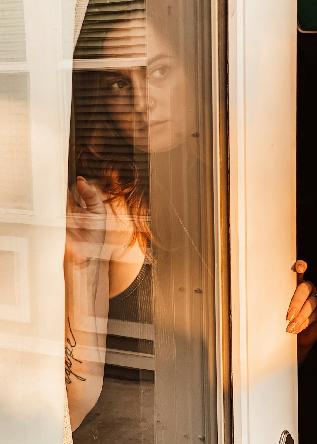 woman in white tank top standing beside white wooden framed glass window