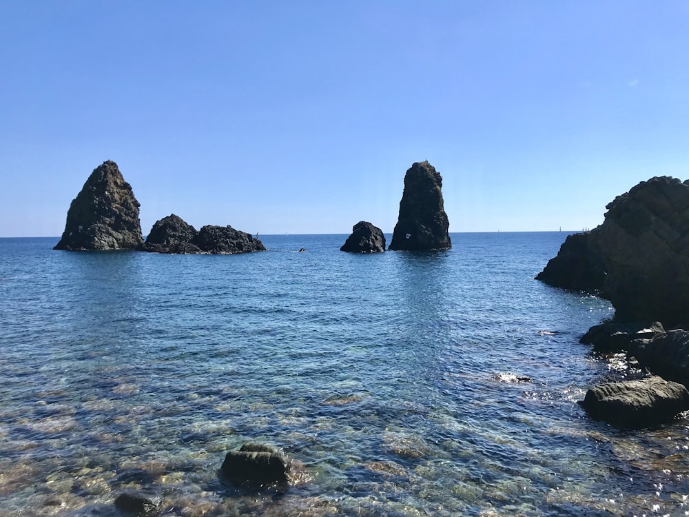 Schwarze Felsformation auf blauem Meer unter blauem Himmel tagsüber