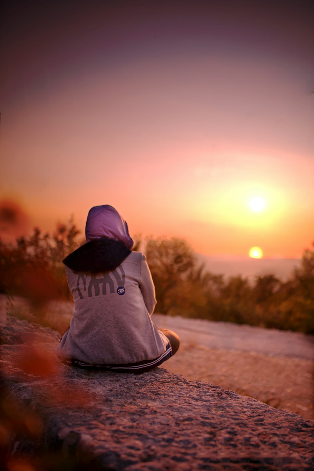 person in gray hoodie sitting on road during sunset