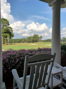 A foldable outdoor rocking chair gently rocking on a porch with a view of trees.