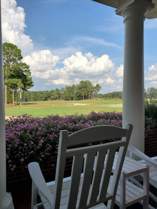 A sunlit porch with rocking chairs overlooking a sprawling southern countryside landscape.