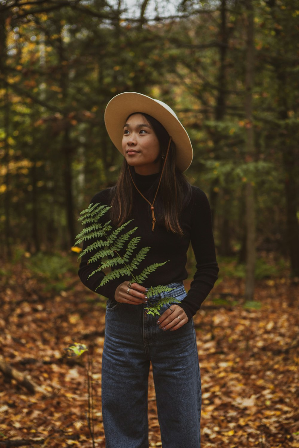 woman in black long sleeve shirt and blue denim jeans wearing brown hat standing near green