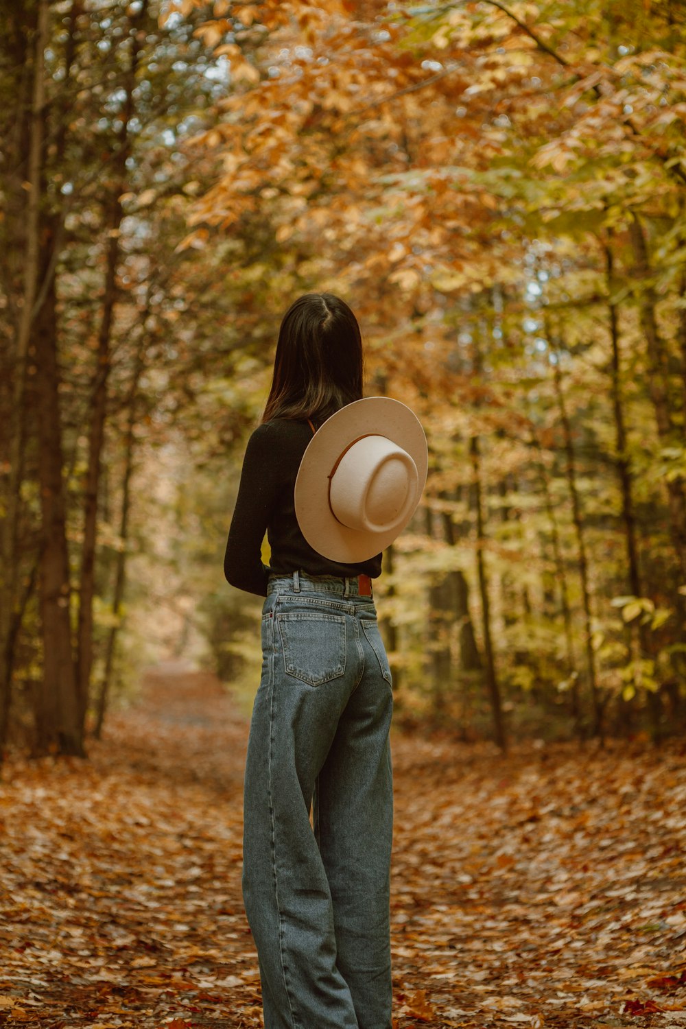 woman in black long sleeve shirt and blue denim jeans standing on forest during daytime