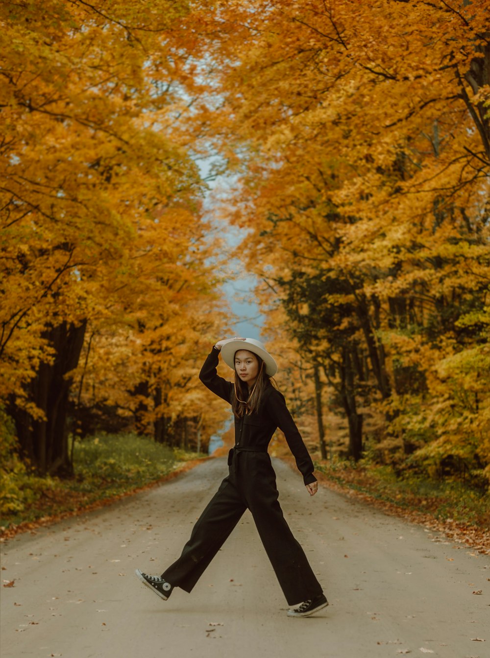 mulher na jaqueta preta e calças pretas andando na estrada entre as árvores durante o dia