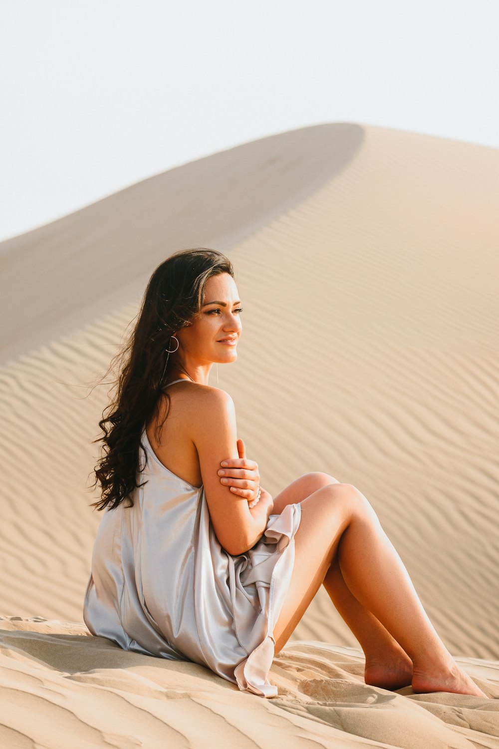 woman in white sleeveless dress wearing black sunglasses standing on sand during daytime