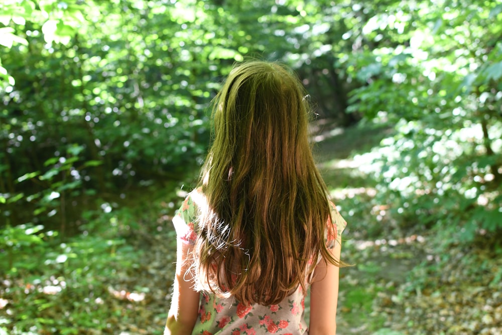 woman in white and red floral dress standing near green trees during daytime