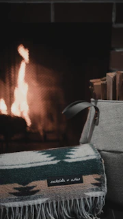 A happy customer unpacking a Nestora storage bag filled with cozy blankets next to a warm fireplace.