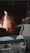 A cozy fireplace setting featuring a burning fire in the background, casting a warm glow. There is a woven blanket with a geometric pattern in shades of green, beige, and white, labeled 'sackcloth + ashes'. Next to it is a canvas basket filled with firewood.