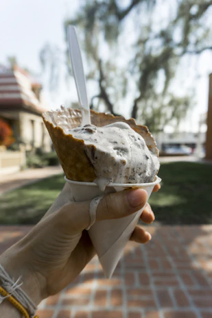 A scoop of creamy vanilla ice cream in a waffle cone, catching the afternoon sun near the concession stand.