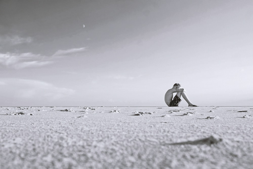 grayscale photo of man sitting on sand