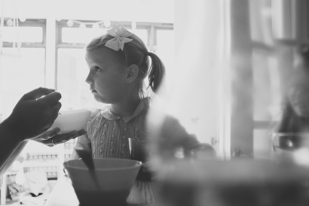 grayscale photo of girl in long sleeve shirt sitting on chair