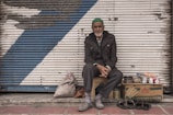 man in black coat sitting on brown wooden bench