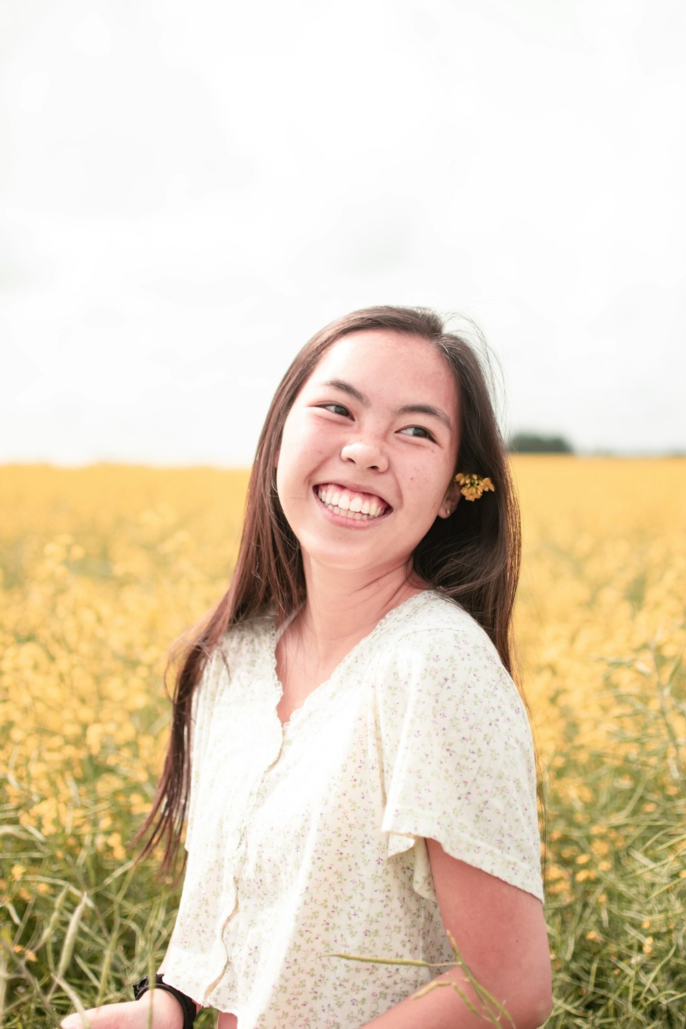 smiling woman in white long sleeve shirt standing on yellow flower field during daytime