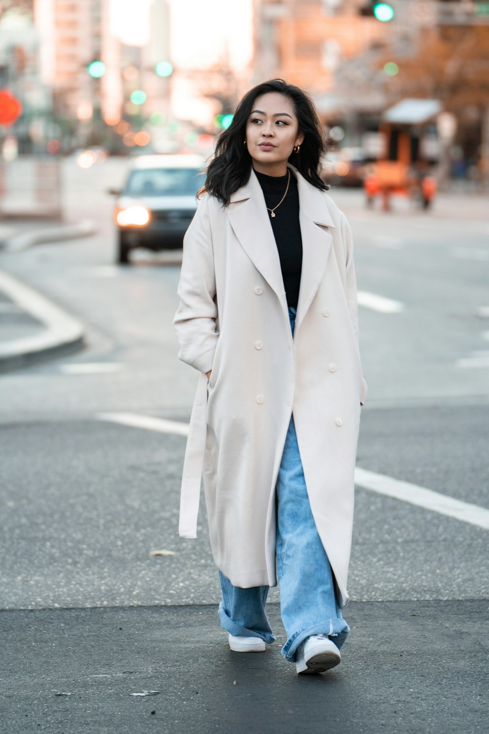 woman in white coat and blue denim jeans standing on road during daytime