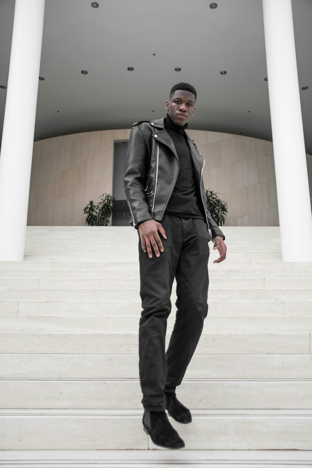 man in black suit jacket and black pants standing on white concrete staircase