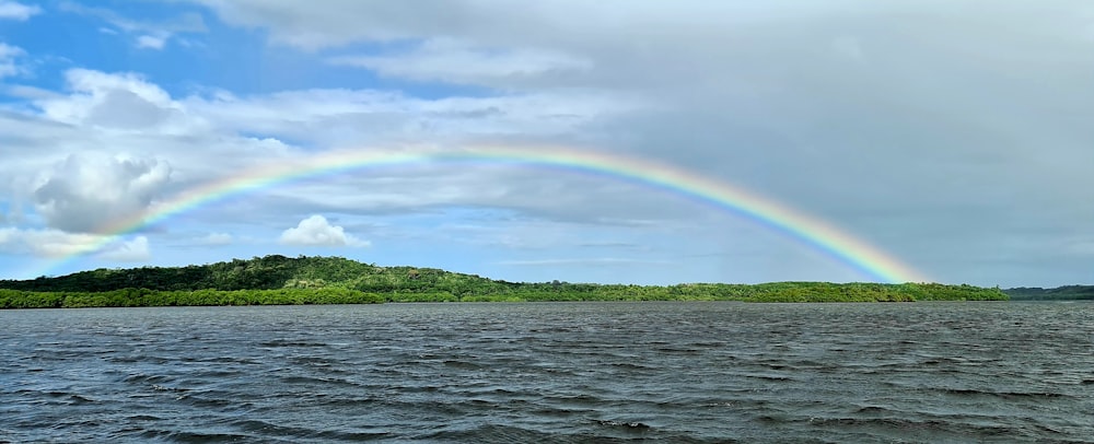 rainbow over green mountain and body of water