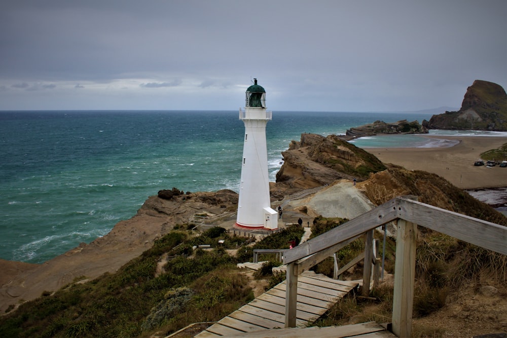 white lighthouse on brown rocky hill near body of water during daytime