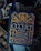 A collection of books with themes related to the occult, witchcraft, and alchemy. The focal point is a book titled 'The Occult Book' by John Michael Greer, featuring ornate gold lettering and symbolic decorations on a dark blue cover. Surrounding the main book are other titles concerning witchcraft, demonology, and magic spells. The overall design is dark and mystical.
