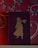A book with a dark cover features a gold silhouette of a person wearing a long dress. The book is placed against a wall with a floral pattern in red, with blue and teal leaves and white swirls.