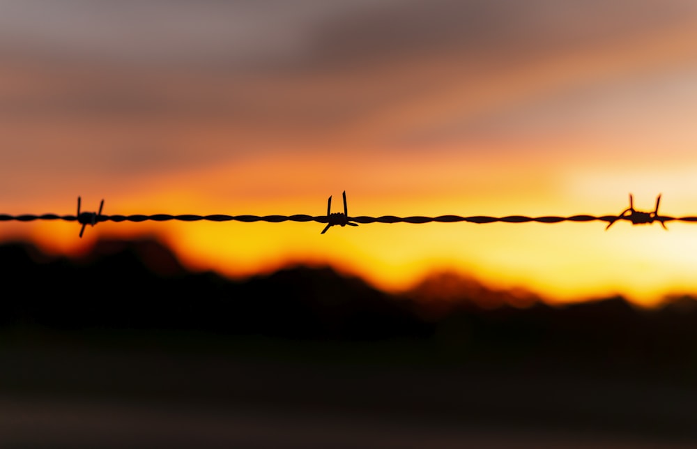 Una cerca de alambre de púas con una puesta de sol en el fondo