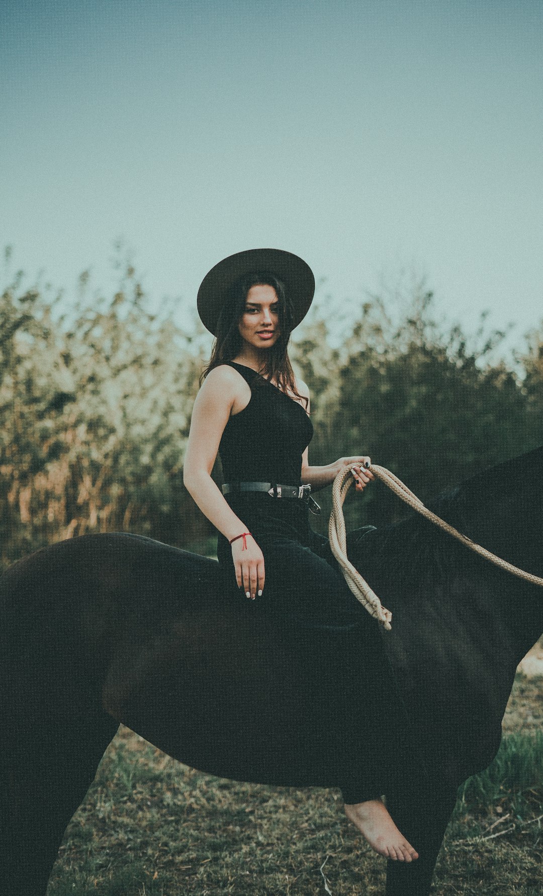 woman in black tank top and black hat riding on black horse during daytime