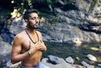 topless man wearing black beaded necklace and blue denim shorts standing on rocky shore during daytime