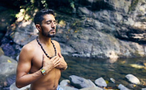 topless man wearing black beaded necklace and blue denim shorts standing on rocky shore during daytime