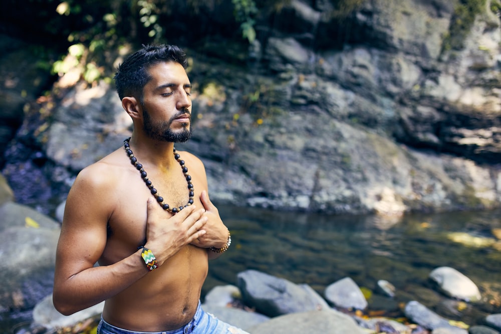 man wearing black beaded necklace and blue denim shorts doing breathwork