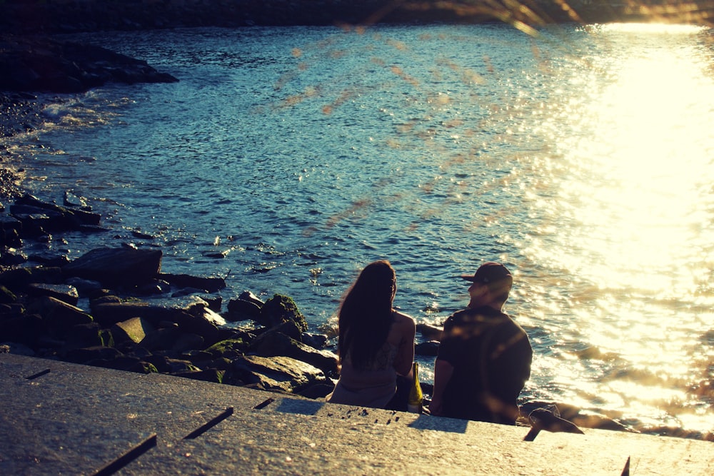 silhouette of people sitting on rock near body of water during daytime