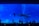A large aquarium tank filled with various species of fish, including a prominent whale shark swimming amid smaller fish. Several silhouetted people stand in the foreground, observing the marine life. The tank is illuminated with a deep blue light, enhancing the aquatic atmosphere.