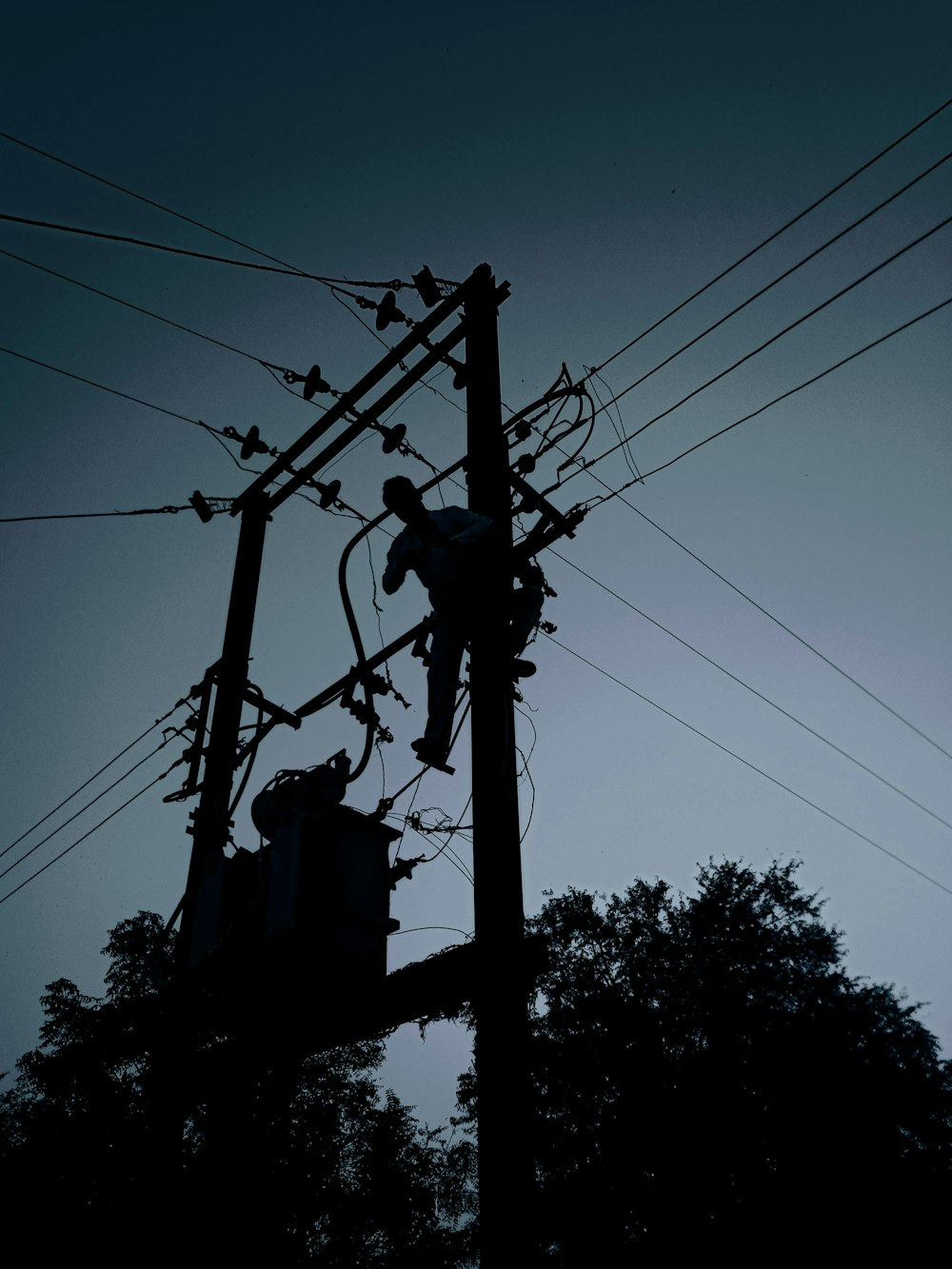 silhouette of electric post under cloudy sky during daytime