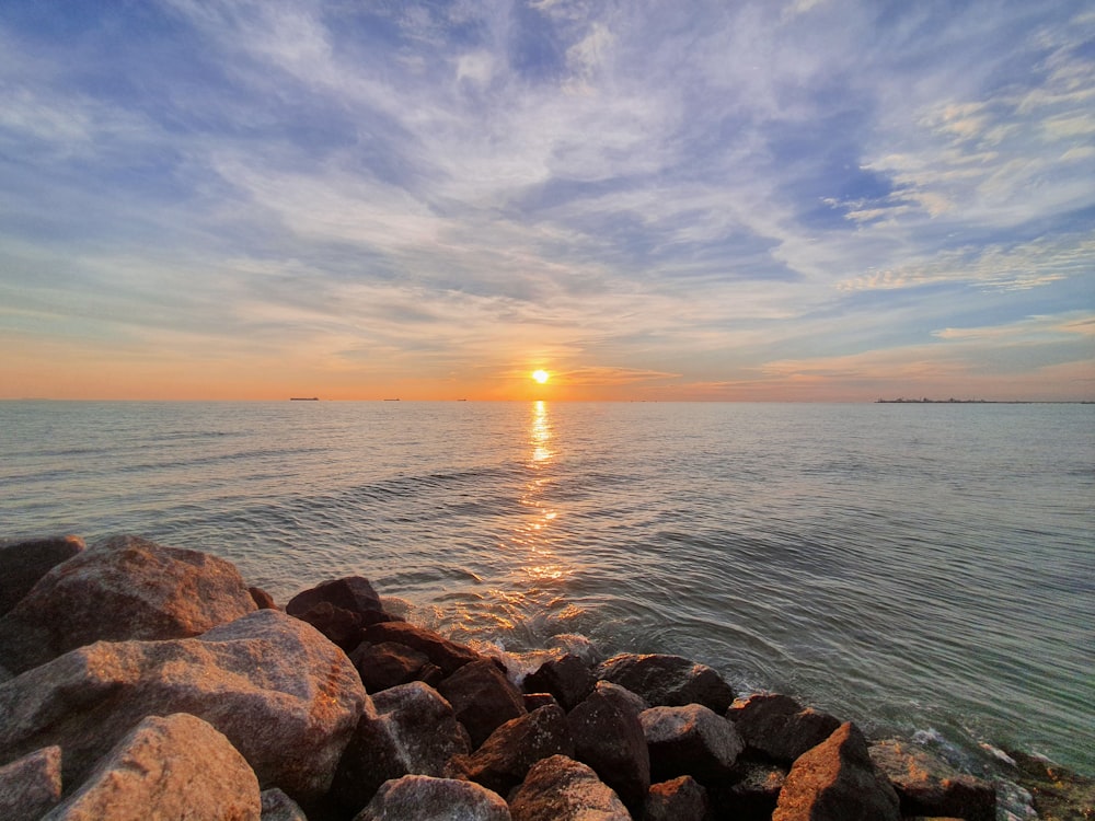 brown and gray rocks near body of water during sunset