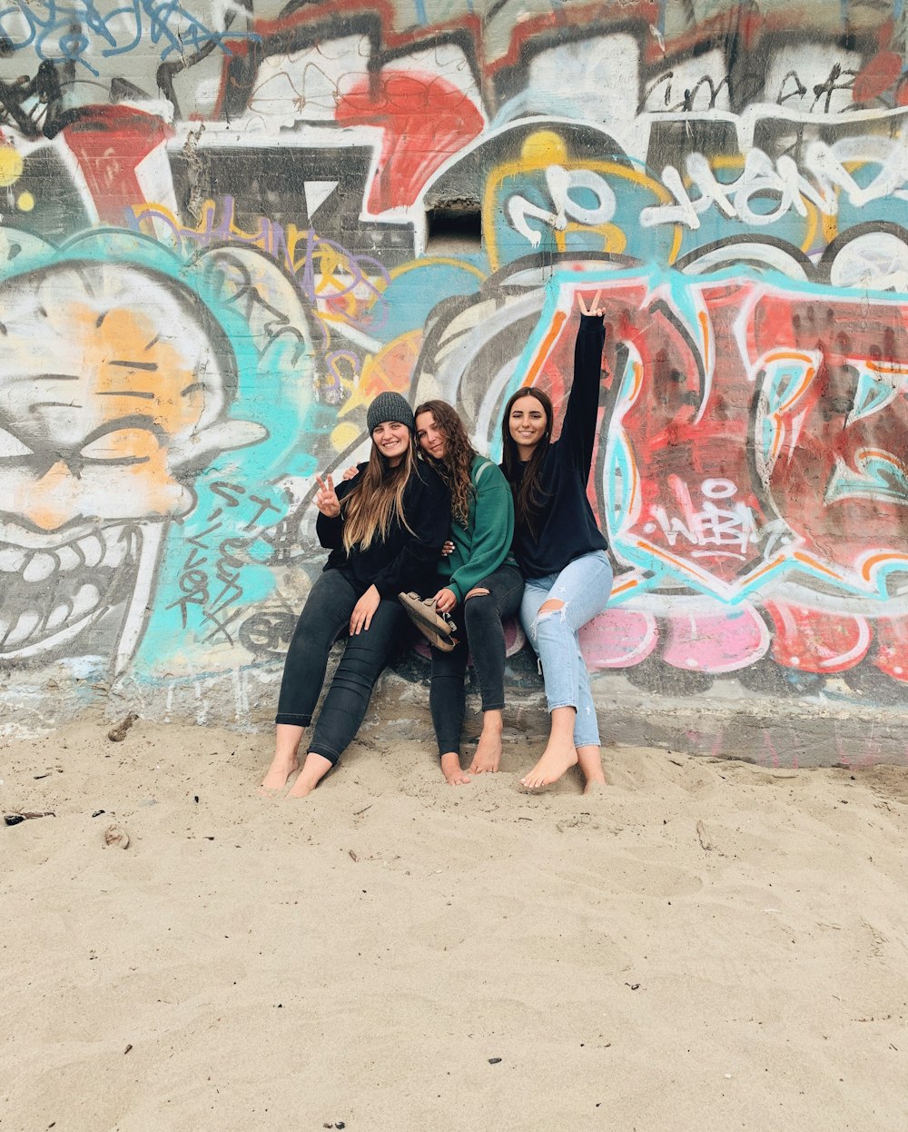 2 women standing beside wall with graffiti during daytime