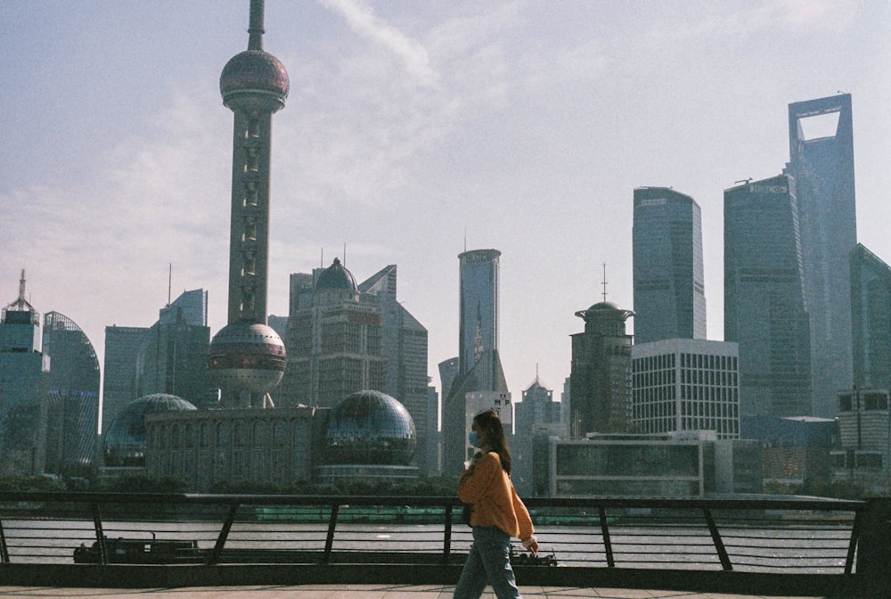 woman in brown jacket sitting on bench looking at city skyline during daytime