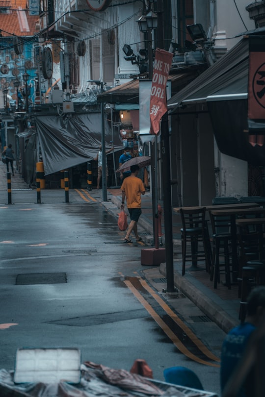 man in orange t-shirt walking on street during daytime in Chinatown Singapore