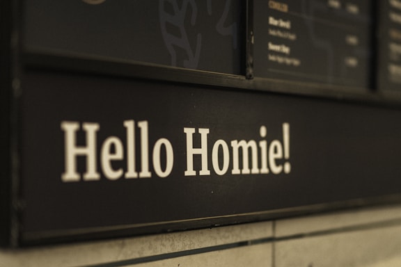 White text on a black background reads 'Hello Homie!' and is part of a menu board in a casual cafe setting.