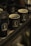 Multiple dark-colored mugs with the logo 'BLING' are placed on a wooden tray. One of the mugs contains coffee beans, and the setting appears to be dimly lit, giving a cozy and rustic feel.