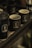 Multiple dark-colored mugs with the logo 'BLING' are placed on a wooden tray. One of the mugs contains coffee beans, and the setting appears to be dimly lit, giving a cozy and rustic feel.