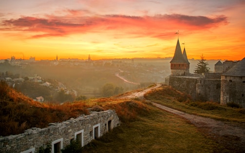 A vibrant fantasy landscape with towering castles and lush forests under a glowing sunset.