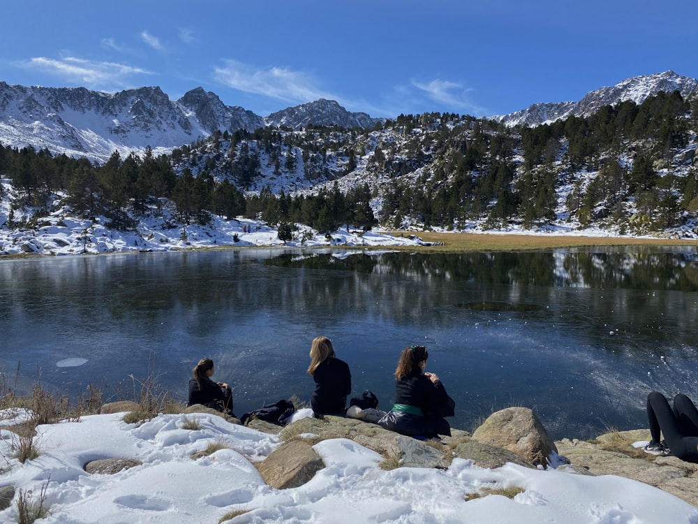 pessoas sentadas na rocha perto do lago durante o dia
