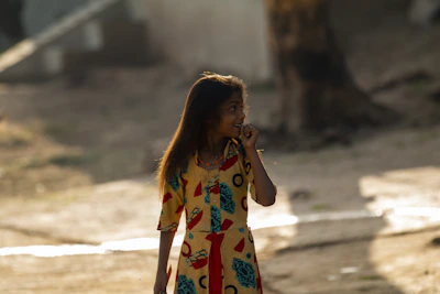 A smiling little girl dressed in a colorful dress with playful patterns, standing in a sunny park