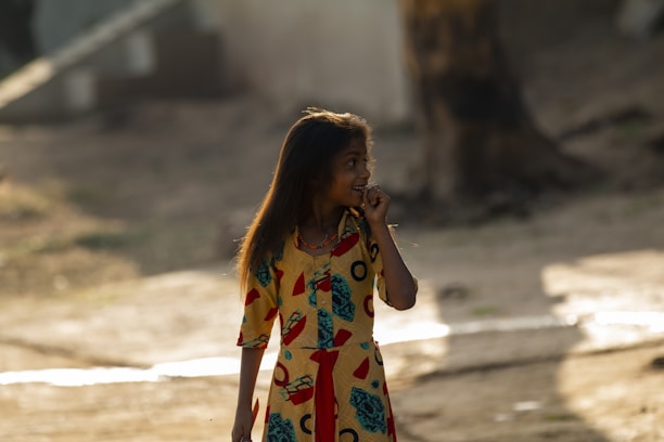A cheerful young girl twirling in a colorful designer dress outdoors on a sunny day.